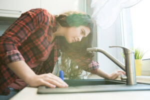 A woman inspecting the kitchen faucet in her home.