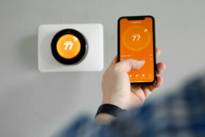 A close-up of a man's hand as he controls a smart thermostat from a phone.