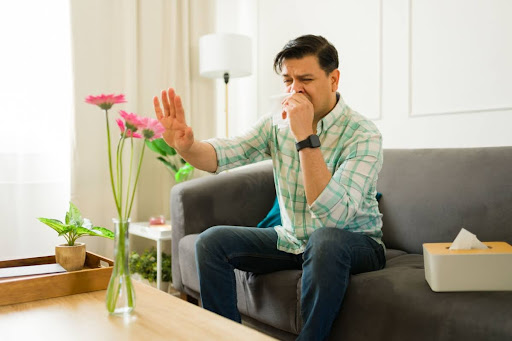 A man with a tissue holding his hand up to a vase with flowers.