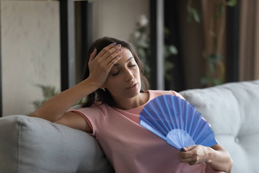 Homeowner sitting on couch with a handheld fan because of broken AC.