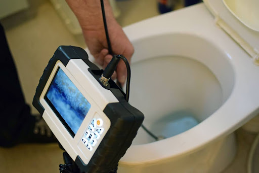 A person inserting a video camera into a toilet.