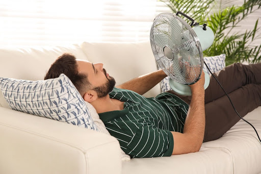 A man holding a fan as he lays on a couch.