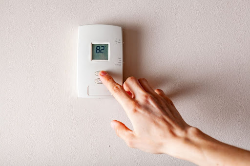 A person touching a button on a thermostat.